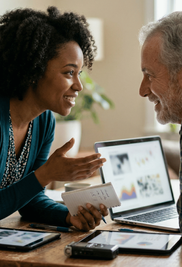 UX Designer de pele escura em reunião de Design Thinking, apresentando insights de pesquisa de usuário (UX Research) em tablet e laptop para stakeholder sênior atento.